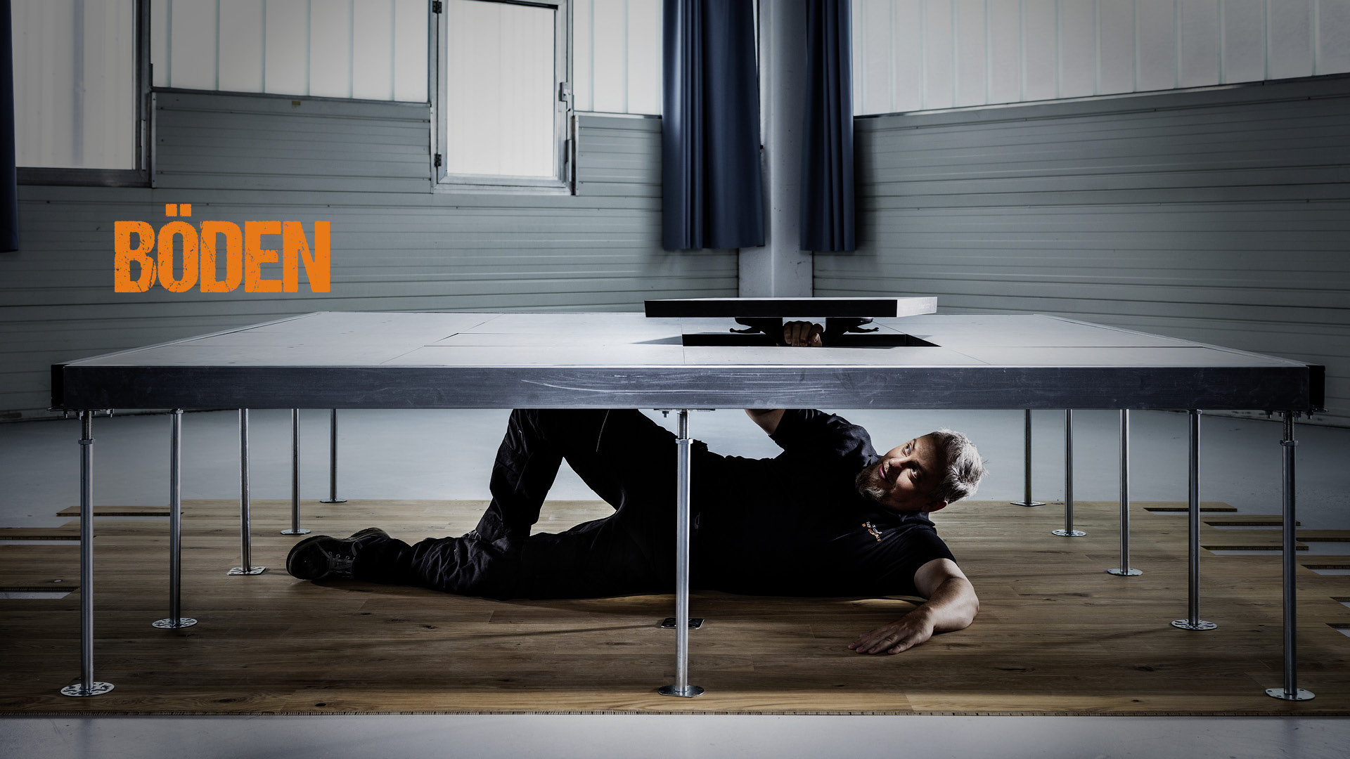 Ronny Schulz von RS Bodentechnik, der Bodenkavalier liegt unter einem Schwerlast-Doppelboden und hebt ein Teilstück davon hoch.