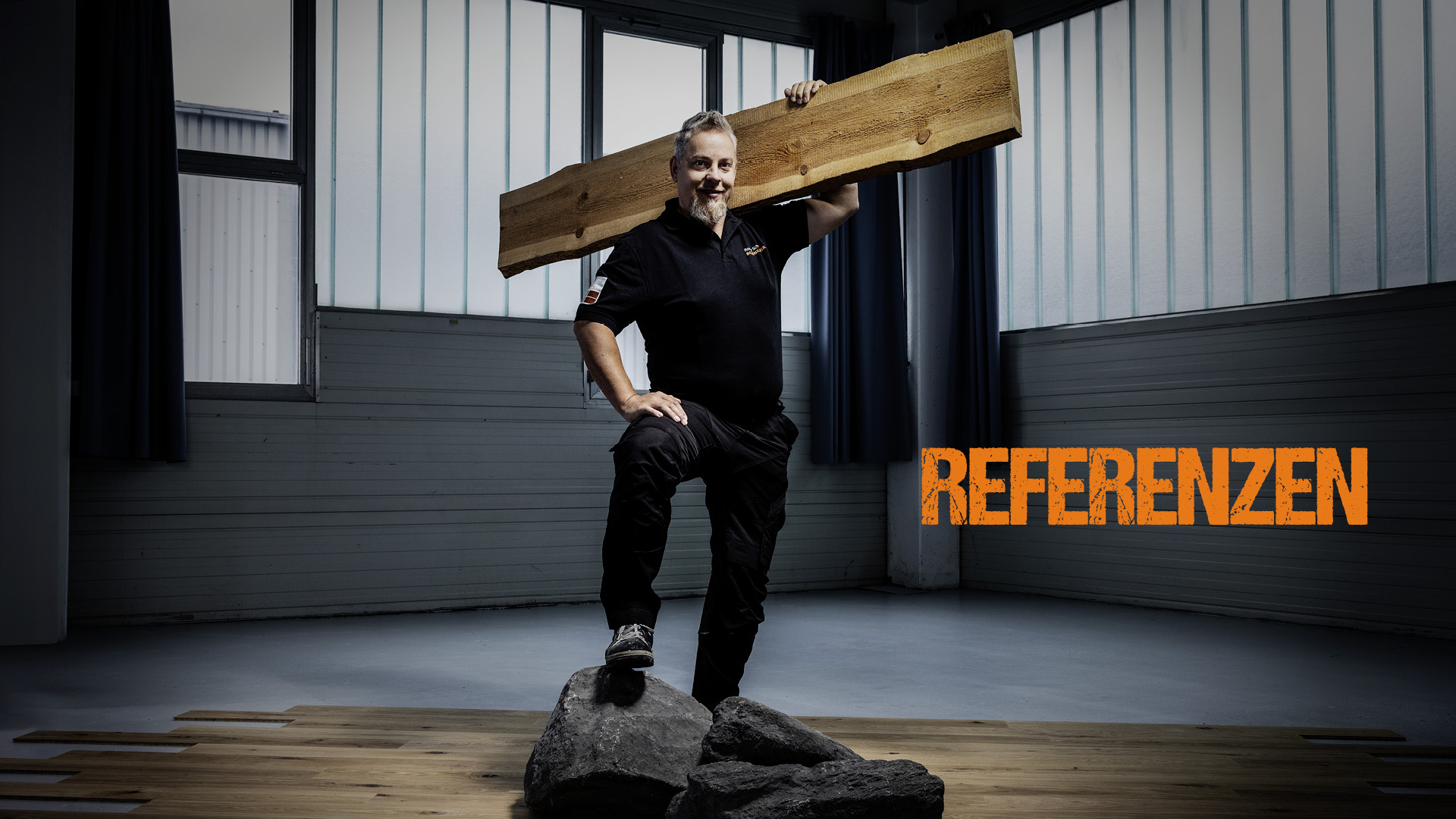 Ronny Schulz von RS Bodentechnik, der Bodenkavalier trägt ein Brett auf der Schulter. Und steht auf einem Felsen. Dieser wiederum auf einem Parkettboden.