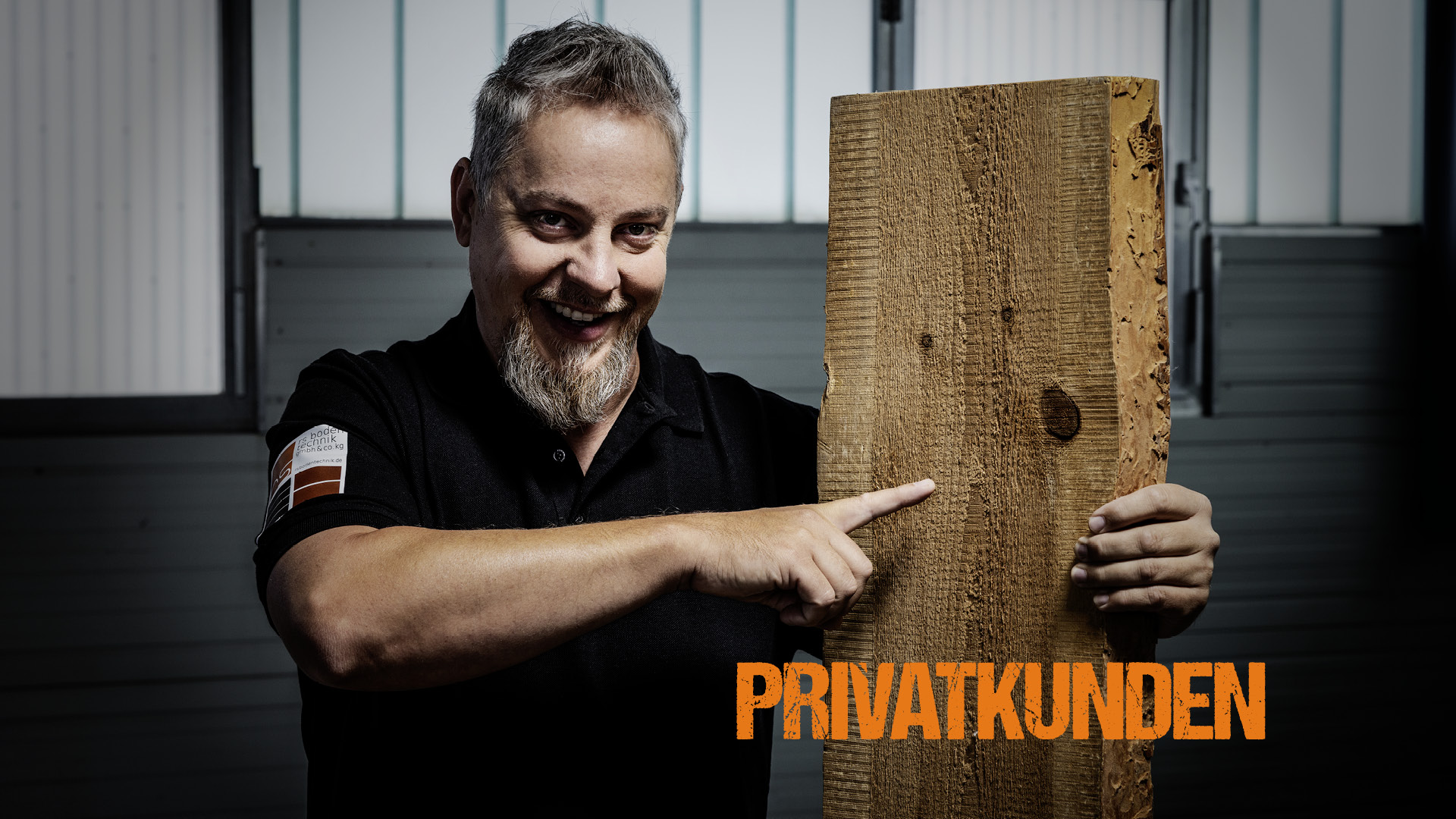 Ronny Schulz von RS Bodentechnik, der Bodenkavalier hält ein Massivholz-Brett senkrecht und deutet mit dem Finger auf die Holzmusterung.